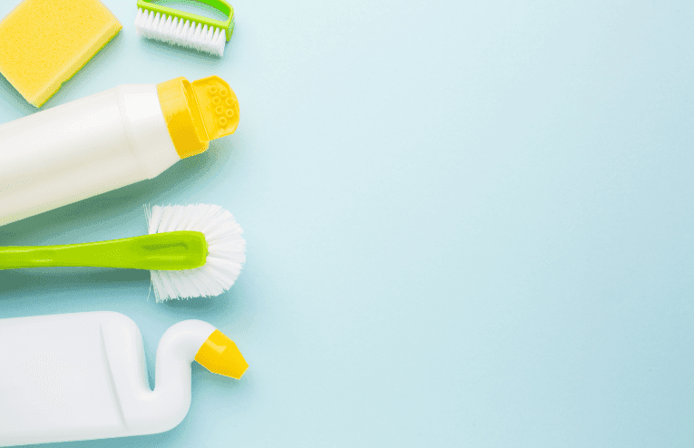 Produits de nettoyage pour WC : brosses, éponge et flacons détergents sur fond bleu.