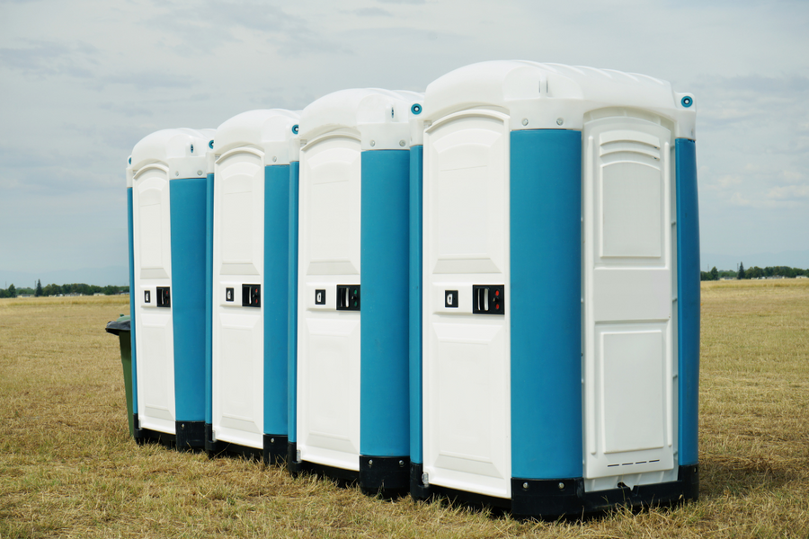 Alignement de toilettes portables bleues et blanches dans un champ d'herbe sèche.