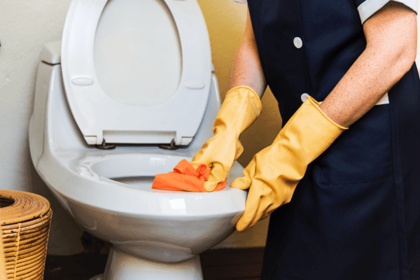 Nettoyage d'une cuvette de WC avec un chiffon et des gants de protection.