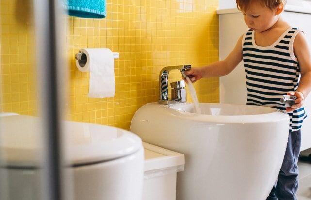 Un jeune enfant utilisant le robinet d'un bidet traditionnel blanc dans une salle de bain.
