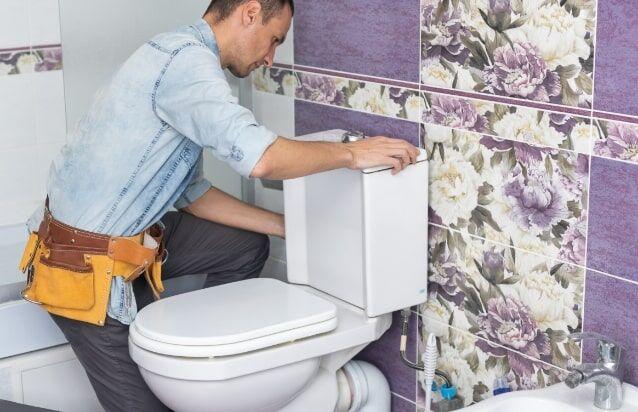 Plombier réparant le mécanisme de chasse d'eau d'un WC blanc.